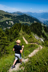 Naklejka na ściany i meble Hiker with poles on a mountain ridge trail with mountain views into the distance
