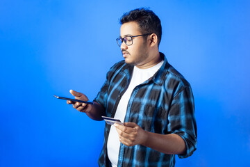 One overweight Indian University student using smart phone and credit card against blue background