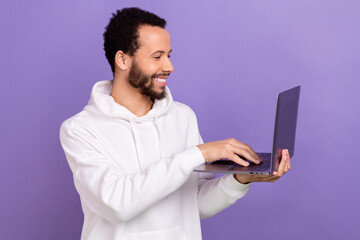 Photo of pleasant smart man curly hairstyle dressed white hoodie look at laptop writing letter isolated on purple color background