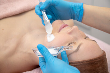 Cropped dermatologist hands in blue gloves applying white peroxide powder with spatula, cream and lotion application