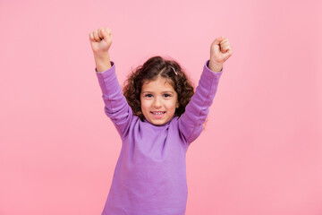 Photo of sweet lucky little child dressed purple pullover smiling rising fists isolated pink color background