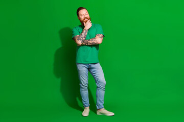 Full length photo of cheerful dreamy guy dressed t-shirt smiling arm chin looking empty space isolated green color background