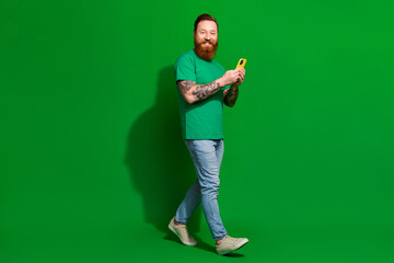Full length photo of positive funky man wear t-shirt texting messages modern gadget isolated green color background