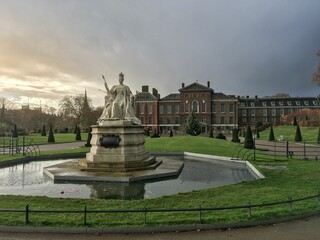 Closeup of a Queen Victoria statue in front of Kensington Palace with a sunset sky view