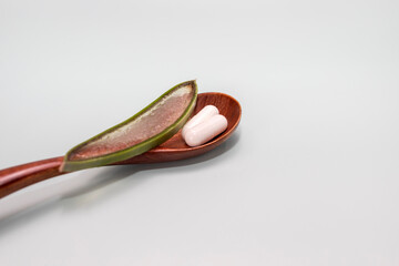 Mockup Wooden Spoon With Capsules And Green Leaf of Aloe Vera On Gray Background. Concept Of Natural Medicine. Copy Space For Text on Right. Horizontal plane. Alternative Medication.