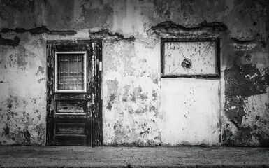 Grayscale of a weathered, wooden door of a cracked wall in an urban area - the concept of poverty