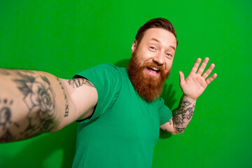 Photo of excited funky guy dressed t-shirt recording vlog waving arm palm isolated green color...