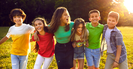 Happy children playing in park and having fun together. Bunch of excited little friends enjoying summer break, walking on sunny meadow and hugging each other. Header, banner. Kids, friendship concept