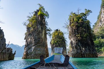 Beautiful scenery of of Cheow lan artificial lake reservoir with karst rock mountains and wooden long tailed boat at sunny day against blue sky in Khao Sok national park of Thailand