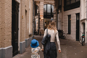 Fototapeta na wymiar Family of mom and child boy looking in future holding hands in summer or spring, back view, rear view, happy family, walking on the street in the city. Fashion style look family.