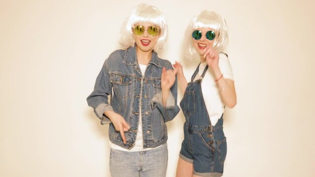 Two young sexy smiling hipster girls in white wigs and red lips. Beautiful trendy women in summer clothes. Carefree models posing in studio. Positive female going crazy
