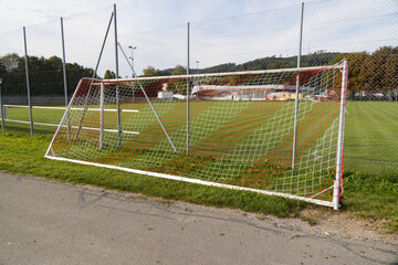 Fototapeta premium empty reserve soccer goal in front of green meadow soccer field. red and white striped net. without people during the day