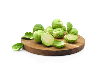 Fresh green brussels sprouts vegetable, whole and halves, on round wooden cutting board isolated on white background    