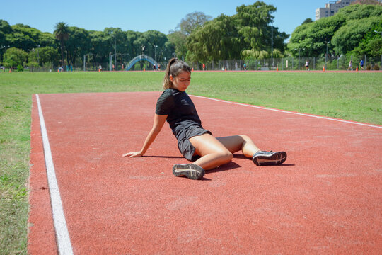 young latin woman on floor doing stretching exercises on running track.