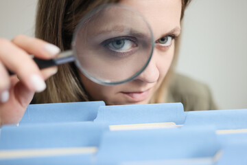 Woman looks through magnifier glass on folders with files