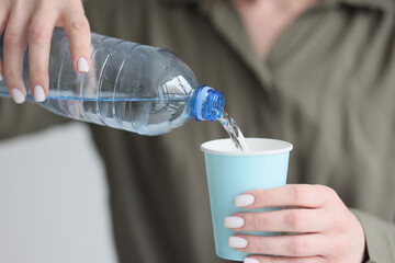 Woman pours clean water from plastic bottle into paper cup