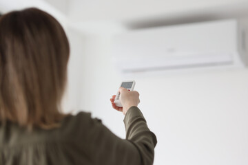 Woman holds remote control turning on air conditioner