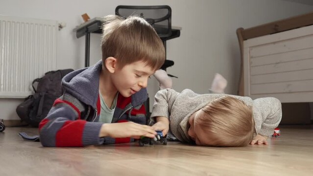 Two boys lying on floor and having a fight with toys. Children playing alone, development and education, games at home