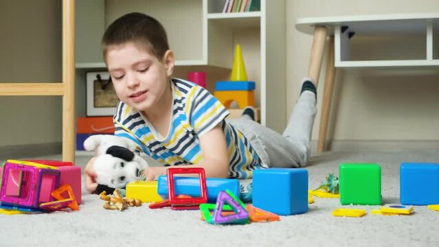 Cute preschool child plays with soft toy dog and other toys lying on the carpet in the children's room