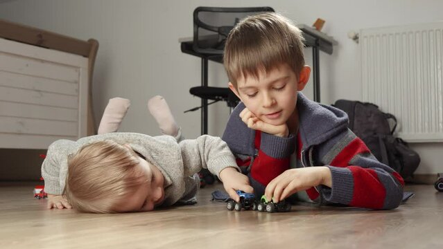 Two brothers lying on floor and palying with colorful toy cars. Children playing alone, development and education, games at home