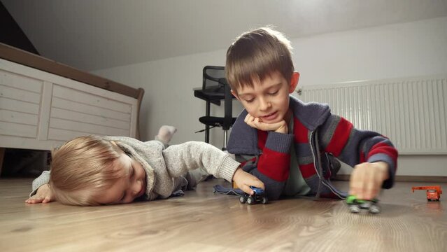 Boy playing with his baby brother with toy cars on floor in bedroom. Children playing alone, development and education, games at home