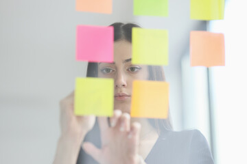 Brunette woman puts sticky notes on glass wall in office