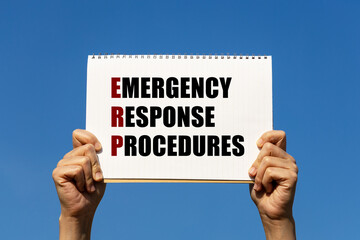 Emergency response procedures text on notebook paper held by 2 hands with isolated blue sky...