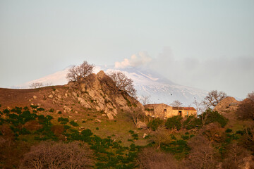 an old rural house on the hill between the pastures and the Volcano Etna in the background in...