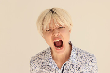 Expressive blonde woman screams with wide open mouth on beige