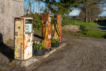 A group of three rusty and disused petrol pumps by the side of a minor road in Wiltshire, UK