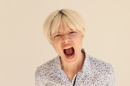 Expressive blonde woman screams with wide open mouth on beige