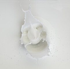 Cosmetic container white lotion droplet fly splashing. Milk lotion pour float to cosmetic bottle. Moisturizer lotion explosion spill. White background isolated high speed shutter freeze top view