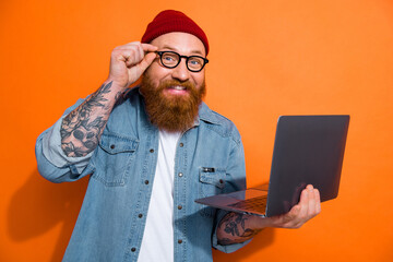 Photo of cheerful positive guy dressed denim jacket eyeglasses texting modern device empty space isolated orange color background