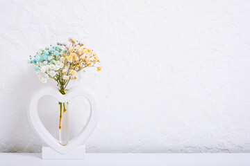 Vase heart-shape with multi-colored gypsophila flowers on white. Minimalistic interior decor with...