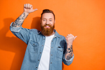 Photo of satisfied young man stylish wearing jacket direct fingers empty space barbershop beard tattoo salon isolated on orange color background