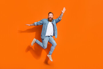 Fototapeta na wymiar Full length photo of cheerful funky guy dressed denim jacket jumping high empty space isolated orange color background