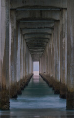 Fototapeta na wymiar Stairway to Heaven: The pillars of the pier steam out towards the ocean like a tunnel as the waves gently lap the shore of a beach in La Jolla, California