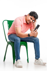 Young indian man sitting on chair and using smartphone on white background.