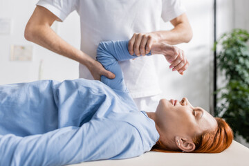 Fototapeta na wymiar chiropractor flexing injured arm of redhead woman in rehabilitation clinic.