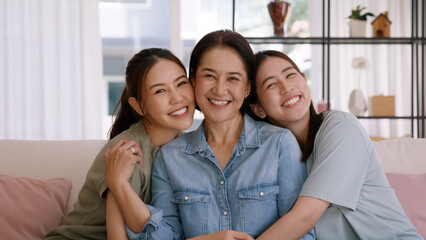Happy good warm time Mother day two grown up kid child looking at camera cuddle hug arm around mature mum. Love kiss care mom asia middle age adult three people smile enjoy sitting easy at home sofa