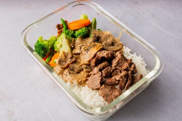 Closeup of cooked beef with a sauce and vegetables in a glass plate