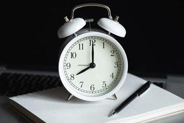 Naklejka premium White alarm clock, notepad and laptop at the workplace, close-up, office work concept, morning at work, deadline.