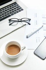 Vertical top view of a white office table with a notebook, glasses and a cup of coffee