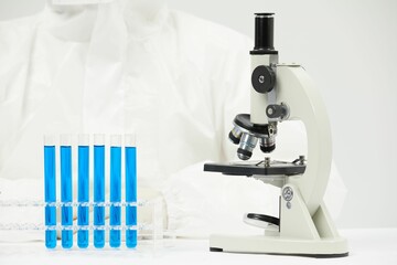Doctor working with an optical microscope in a medical laboratory with test tubes on the table