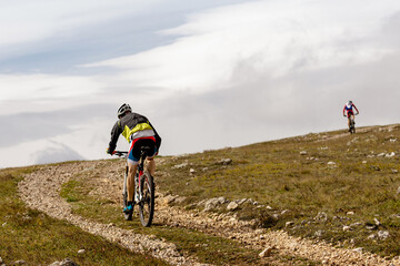 back male cyclist riding mountain bike on mountain gravel road in cross-country cycling race