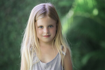 Candid outdoor portrait of adorable 5 years old girl with greenery in the background
