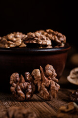 Organic dried walnut kernels next to the ceramic bowl on a dark wooden table. Walnut kernels close up.