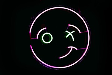 Neon sign of a winking emoji in Madrid Spain isolated on an empty black background