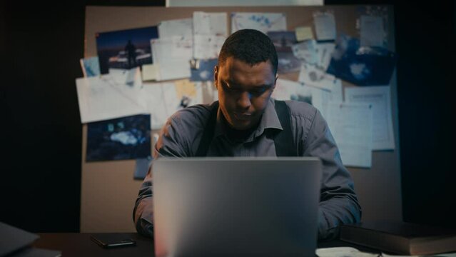 African American policeman looking at laptop in his office, private investigator