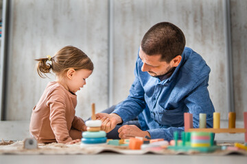 Naklejka premium One man caucasian playing at home with his daughter toddler on the floor with wooden toys, modern parenthood lifestyle single parent concept 